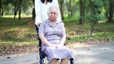 亚洲老年或老年妇女，在公园度假时在轮椅上得到照顾、帮助和支持：健康强壮的医疗。
